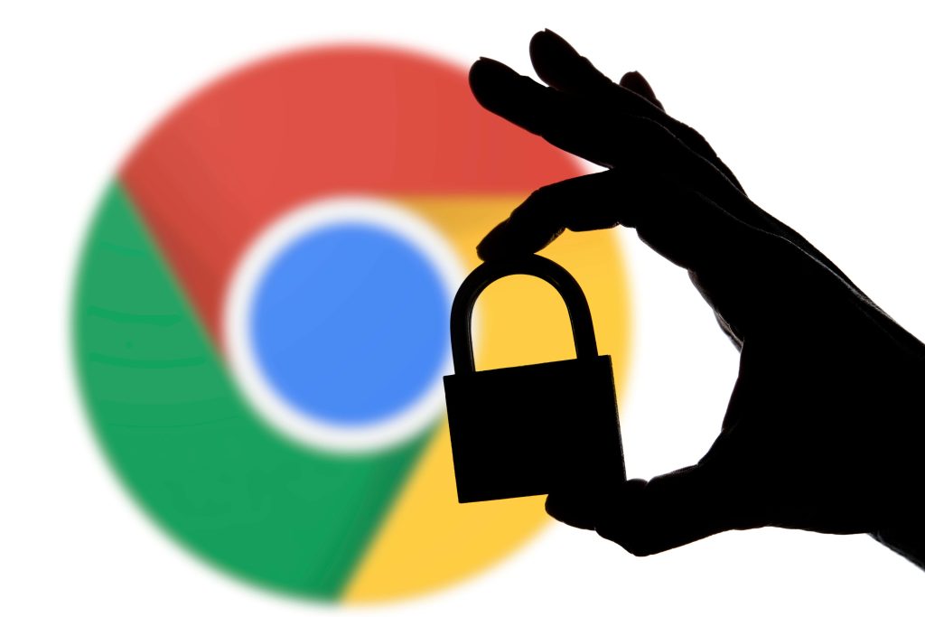 A silhouette of a hand holding a padlock in front of a blurred Google Chrome logo, symbolizing online security and privacy.