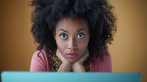 A woman with wide eyes, staring intensely at a screen, conveying a sense of shock or surprise, possibly due to unexpected or startling information.