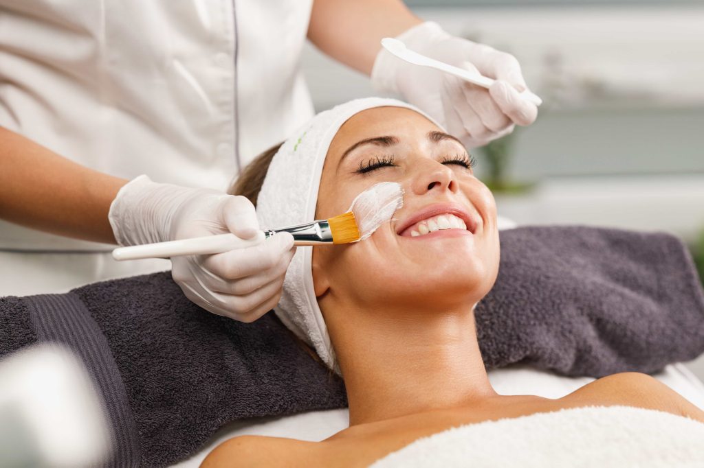 A woman enjoying a facial treatment at a spa with a face mask being applied by a professional.