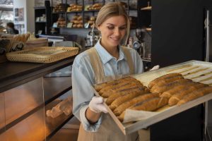 A smiling baker holding a tray of freshly baked bread inside a local bakery, highlighting personalized service and quality in small businesses.