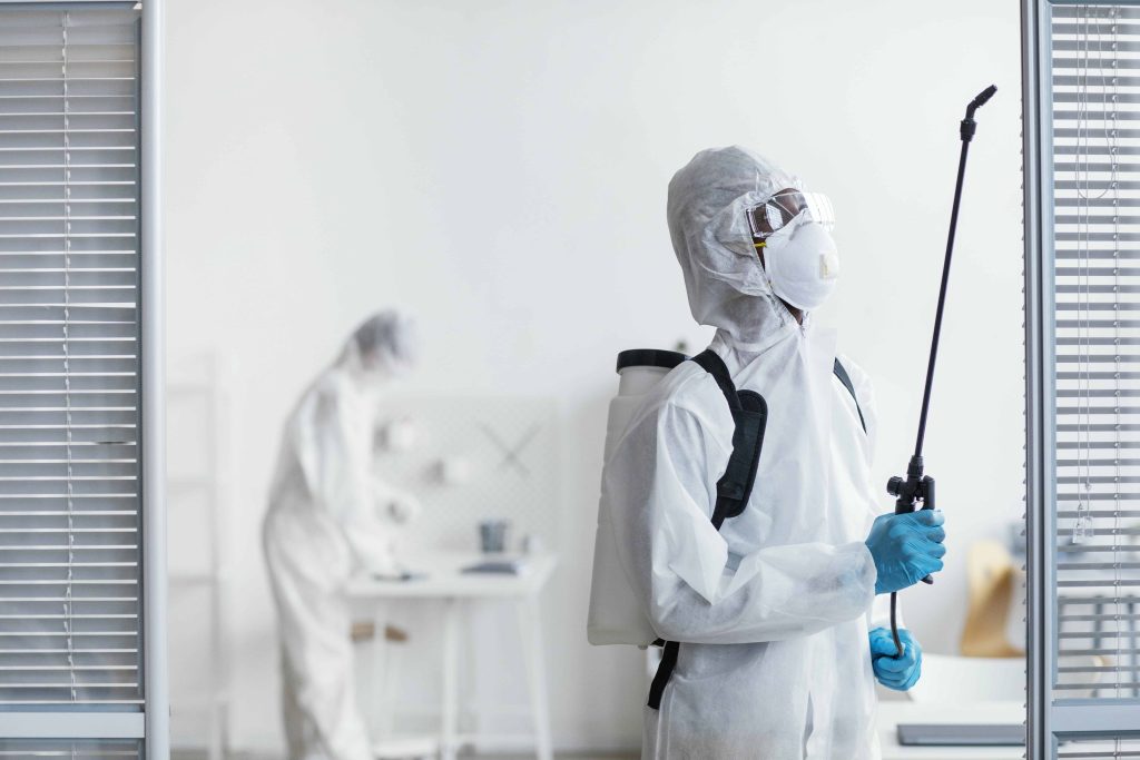 A pest control worker in full protective gear, using a sprayer to treat an indoor area, representing professionalism and thoroughness in pest management services.