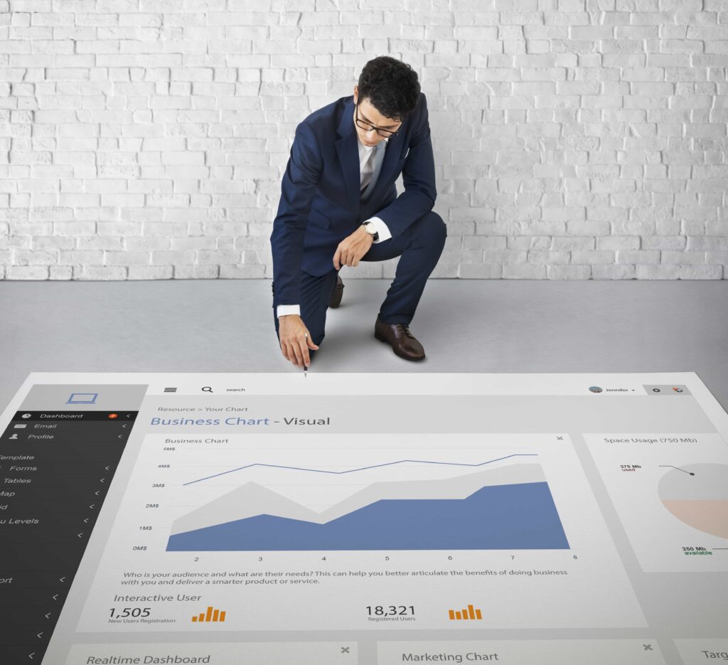 Man in a suit kneeling down reading graph of trends